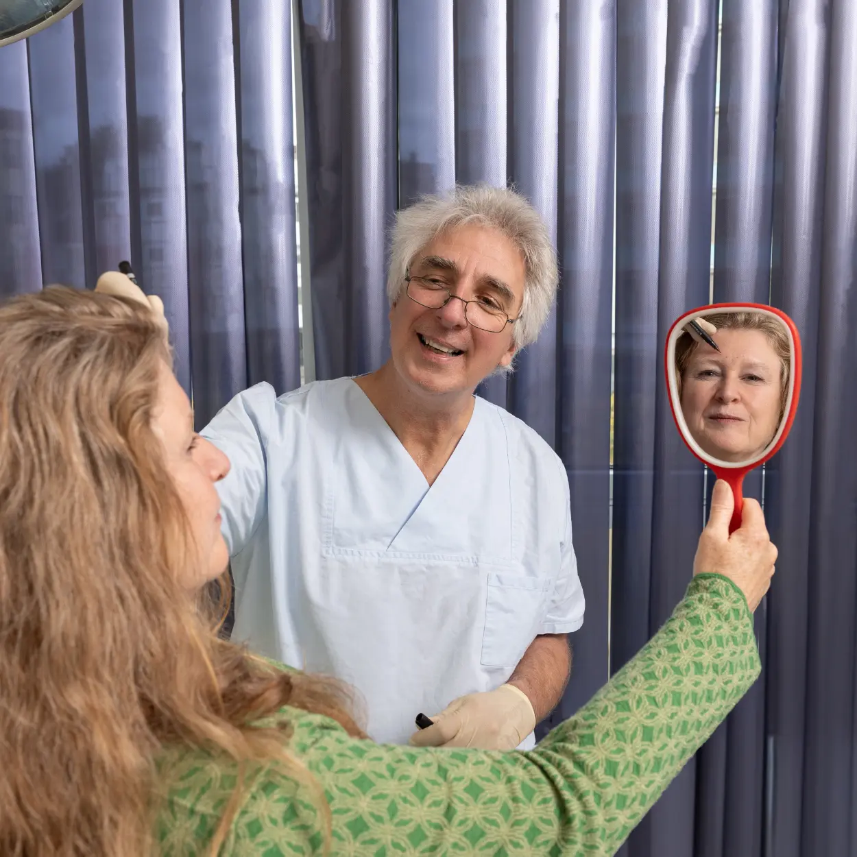 Patientin hält Spiegel hoch während Dr Wahn etwas erklärt | Gemeinschaftspraxis Dr. Dr. Jürgen Wahn - Dr. Dr. Tassilo Illg